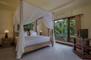 a bedroom with a canopy bed and a tv at Puri Astina Villa in Ubud