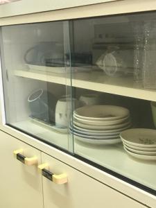 une armoire en verre avec des assiettes et de la vaisselle dans l'établissement Joyful Rose, à Ginowan