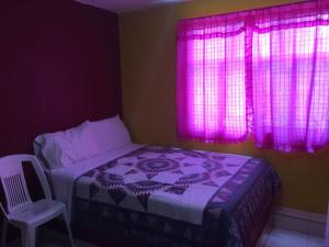 a bedroom with a bed and pink curtains and a chair at Hotel Economico in Xilitla
