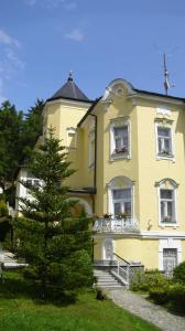 Una casa amarilla con un árbol delante. en Villa Sonnenstrahl en Mariánské Lázně