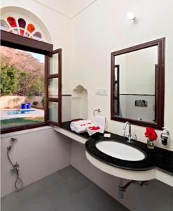 ein Bad mit einem Waschbecken, einem Spiegel und einem Fenster in der Unterkunft DhulaGarh A Heritage Hotel in Bānskhoh