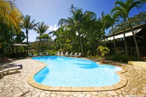 Una piscina en un resort con sillas y palmeras. en Hotel - Résidence Habitation Grande Anse, en Deshaies