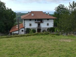 a white house on a hill with a field at Casa Rural Endeitxe in Ereño