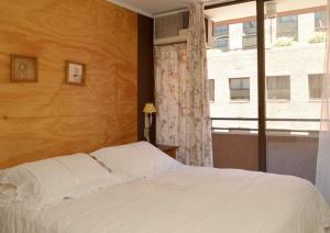 um quarto com uma cama branca e uma janela em Encomenderos Suites - Apartamentos Amoblados em Santiago