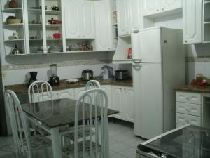 a white kitchen with a table and a refrigerator at Itaguá Guest House in Ubatuba