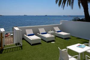 une terrasse avec des chaises, des tables et l'eau dans l'établissement Enkala Apartamentos, à Ibiza