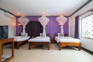 three beds in a room with purple walls and a tv at Tan Kang Angkor Hotel in Siem Reap