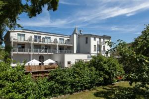 a large white building with a balcony and trees at Waldhotel in Graal-Müritz