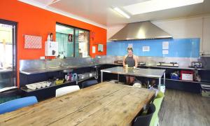a woman standing in a kitchen with a wooden table at Aussitel Backpackers in Coffs Harbour