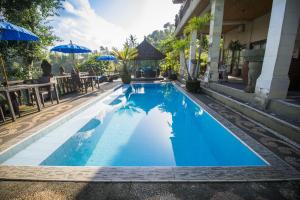 a large blue swimming pool with tables and umbrellas at Villa Kalisat Resort in Ubud