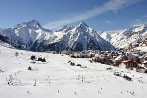 Vacancéole - Résidence Alpina Lodge في لي دوز آلب: مجموعة من الناس يتزحلق على جبل مغطى بالثلج