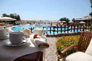 a table with two cups of coffee and towels next to a pool at Hotel Resort Nuraghe Arvu in Cala Gonone