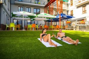 Ein Mann und eine Frau in Badeanzügen, die auf Gras sitzen in der Unterkunft Hotel Kamilla in Balmazújváros