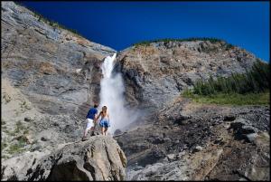 a man and woman standing on a rock in front of a waterfall at Cathedral Mountain Lodge in Field