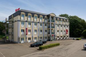 un gran edificio blanco con coches aparcados en un aparcamiento en ibis Liège Seraing en Boncelles