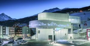 a building with cars parked in a parking lot with mountains at Hotel Garni Ehrenreich in Sölden