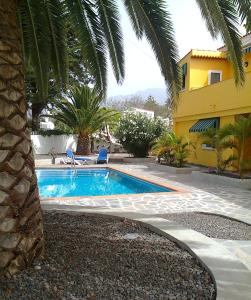 a swimming pool next to a house with a palm tree at Apartamentos Villa María in Los Llanos de Aridane