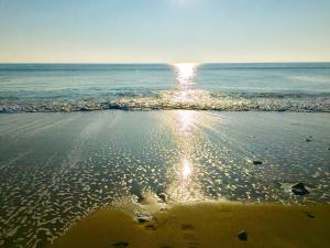 a beach with the sun reflecting on the water at Hôtel Restaurant & Spa Plaisir in Le Bois-Plage-en-Ré