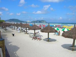 - une plage avec des parasols et des personnes assises sur le sable dans l'établissement COMFORT GUARUJÁ ENSEADA APARTMENT 26 WIFI, GARAGEM e AR CONDICIONADO, à Guarujá