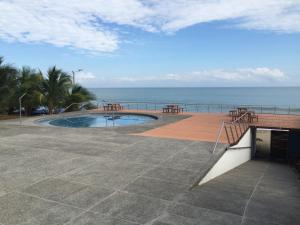 a patio with a pool and tables and the ocean at Suite frente al mar in Tonsupa