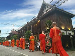 a group of men in orange robes walking down a street at Ancient Luangprabang Hotel in Luang Prabang