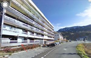 a large building with cars parked on the side of a street at Appart Eterlou Chamrousse in Chamrousse