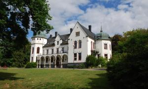 uma grande casa branca com telhados verdes em Hellidens Slott och Vandrarhem em Tidaholm
