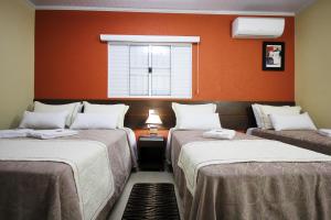 two beds in a room with an orange wall at Pousada Recanto Solar dos Pássaros in Olímpia +36 photos