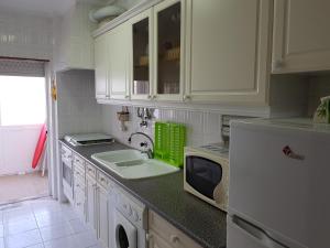 アルマカオ・デ・ペラにあるBeira Mar Terrace Apartmentの白いキャビネット、シンク、冷蔵庫付きのキッチンが備わります。