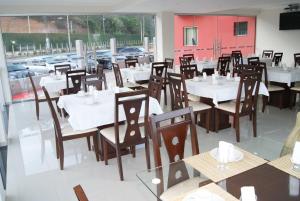 a dining room with white tables and wooden chairs at Hotel Nardy in Alvinópolis
