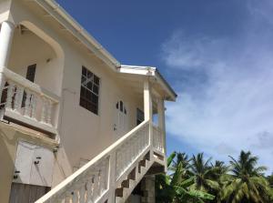 a white house with a balcony and palm trees at Coconut cottage in Bridgetown