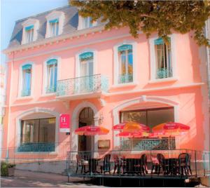 ein rosafarbenes Gebäude mit Tischen und Sonnenschirmen davor in der Unterkunft Hôtel De France in Chalabre