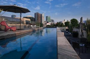 a swimming pool with an umbrella and chairs and a building at Las Suites Campos Eliseos in Mexico City