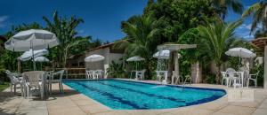 a swimming pool with white chairs and umbrellas at Pousada Areia Preta in Cumuruxatiba