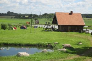 a cabin in the middle of a field with a pond at Krustceles in Baltinava +12 photos