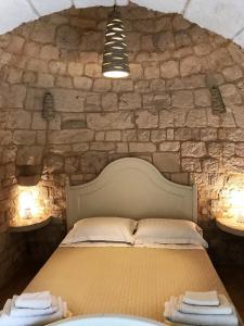 1 dormitorio con pared de piedra, 1 cama y 2 luces en Agritrulli en Ostuni