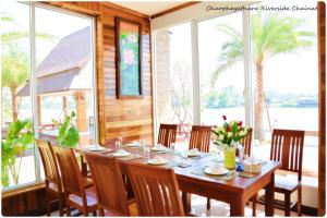 a dining room with a table and chairs and windows at Chaophayathara Riverside Hotel in Chai Nat