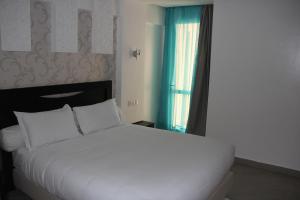 1 dormitorio con cama blanca y ventana en Résidence La Place, en Laayoune