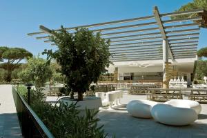 a patio with white chairs and a tree in front of a building at Camping Village Roma Capitol in Ostia Antica