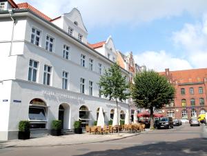 ein weißes Gebäude mit Tischen und Stühlen auf einer Straße in der Unterkunft Hotel Schweriner Hof in Stralsund