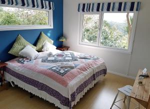a bedroom with a bed with blue walls and two windows at Fernglen B&B in Auckland