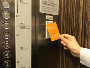 a person holding an orange card in front of an elevator at Hakata Green Hotel Annex in Fukuoka