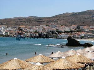 a beach with umbrellas and people in the water at Vassiliki Studios in Andros