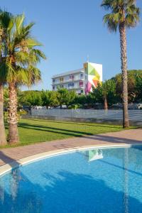 a swimming pool with palm trees and a building at Càmping Bellsol in Pineda de Mar