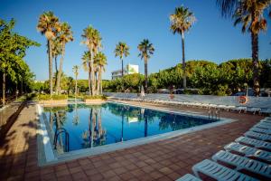 a swimming pool with palm trees and chairs at Càmping Bellsol in Pineda de Mar