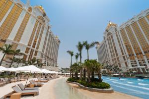 a resort pool with chairs and palm trees and buildings at Hotel Okura Macau in Macau