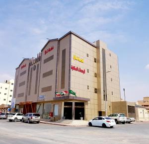 Un gran edificio con coches aparcados en un estacionamiento. en فضة تالا للشقق المخدومة 1, en Buraidah