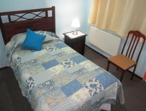 a bedroom with a bed with a blue pillow and a chair at Hostal Andalue Temuco in Temuco
