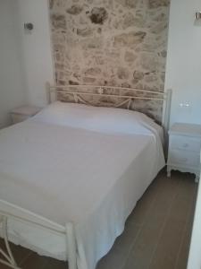 Cama blanca en habitación con pared de piedra en Villa Magda, en Makrádes