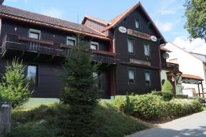 Una casa negra con un árbol delante. en Pension Jagdhütte en Sankt Andreasberg